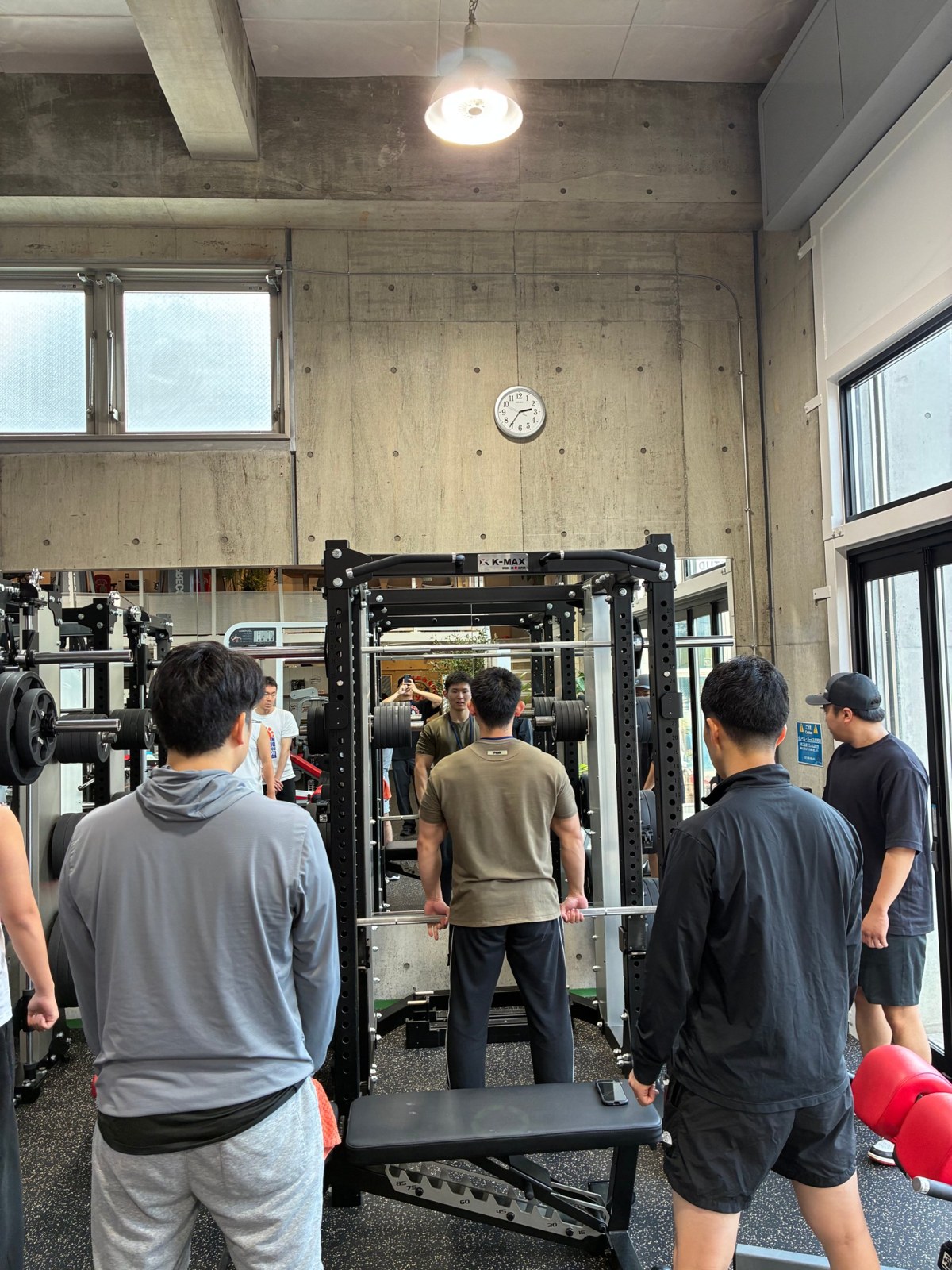 デッドリフトの動きを見せるトレーナーと、まわりで見学する参加者